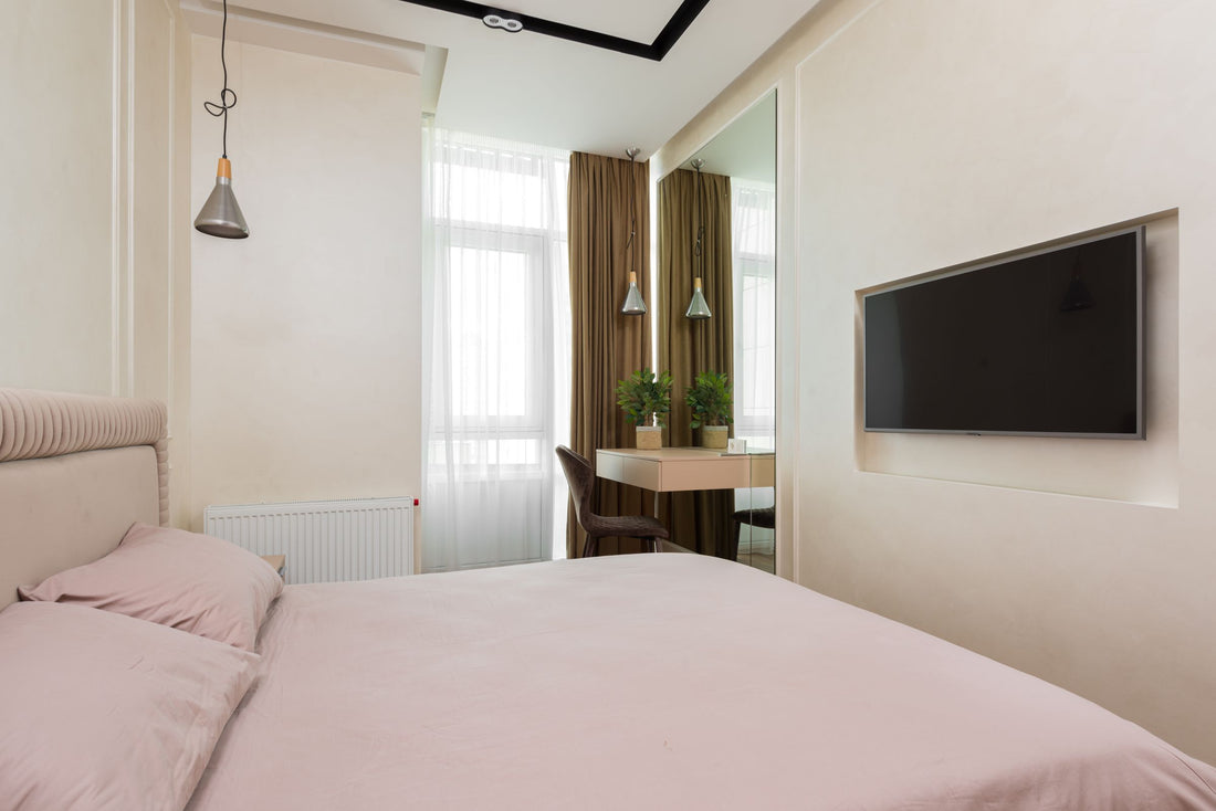 Petite chambre compacte et bien rangée avec lit, miroir et fenêtre habillée de rideaux