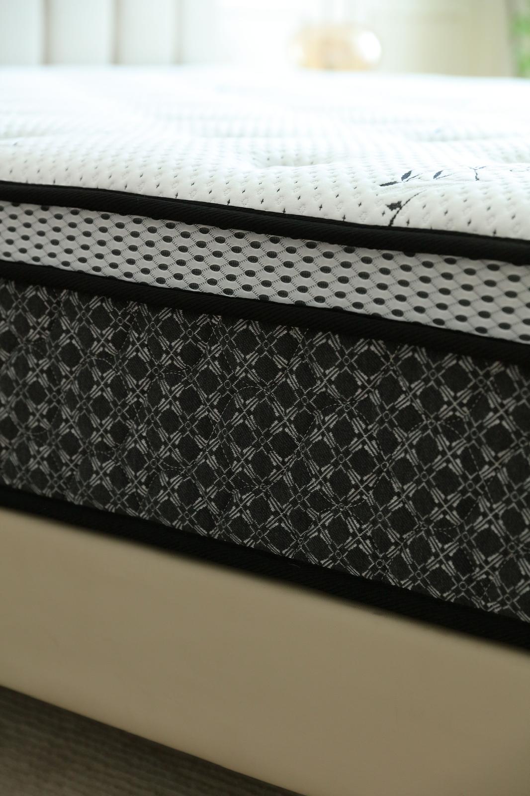 Gros plan sur l'épaisseur du matelas Royal : surface matelassée blanche et bandeau latéral noir à motifs